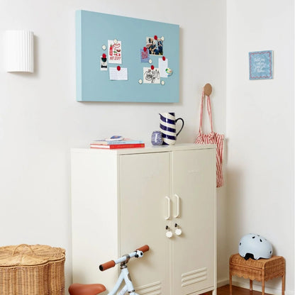 Children's room with a white cabinet, bike, and decorative items on a light blue wall.