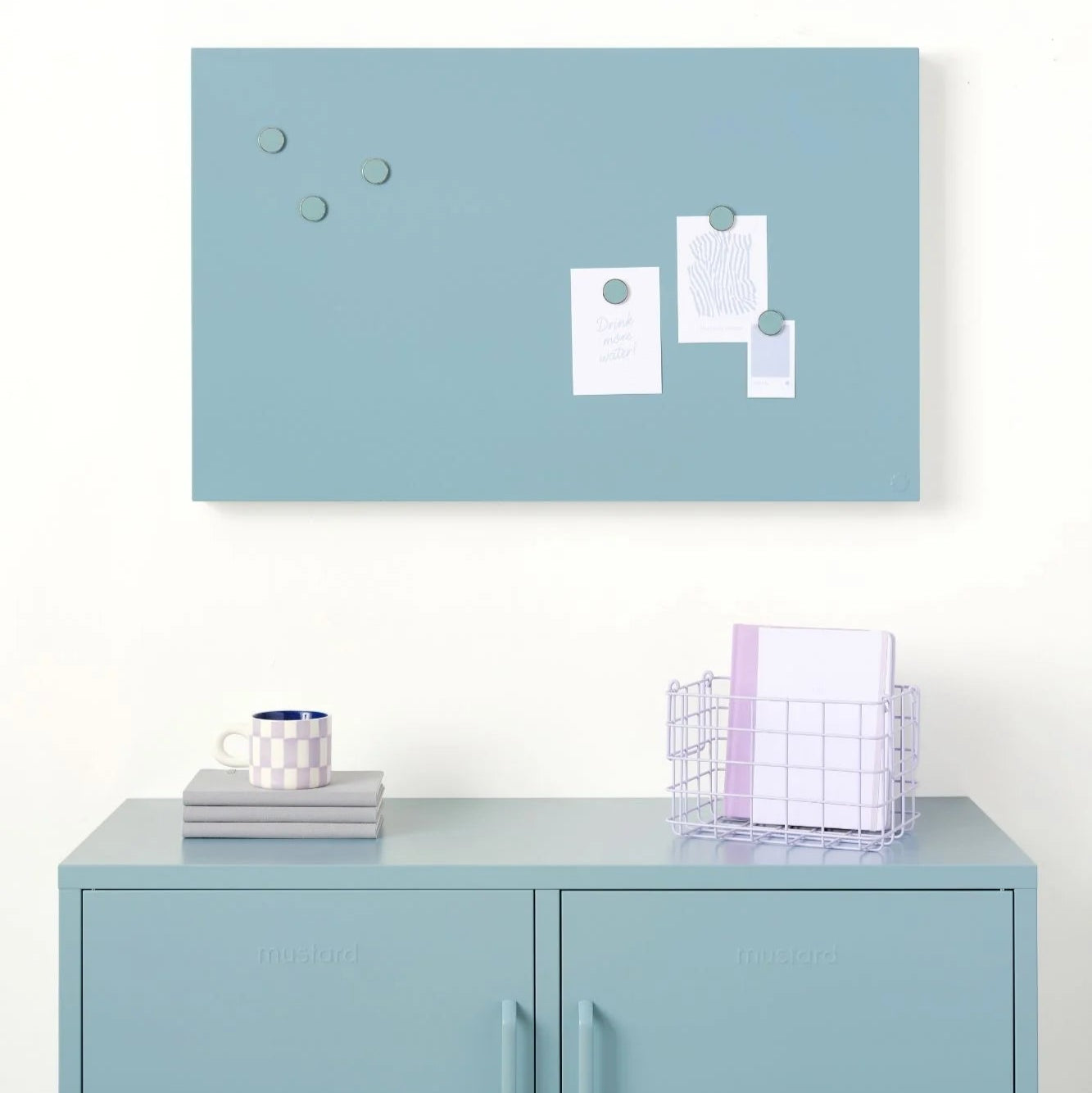 Light blue cork bulletin board with magnetic clips on a white wall above a light blue locker.