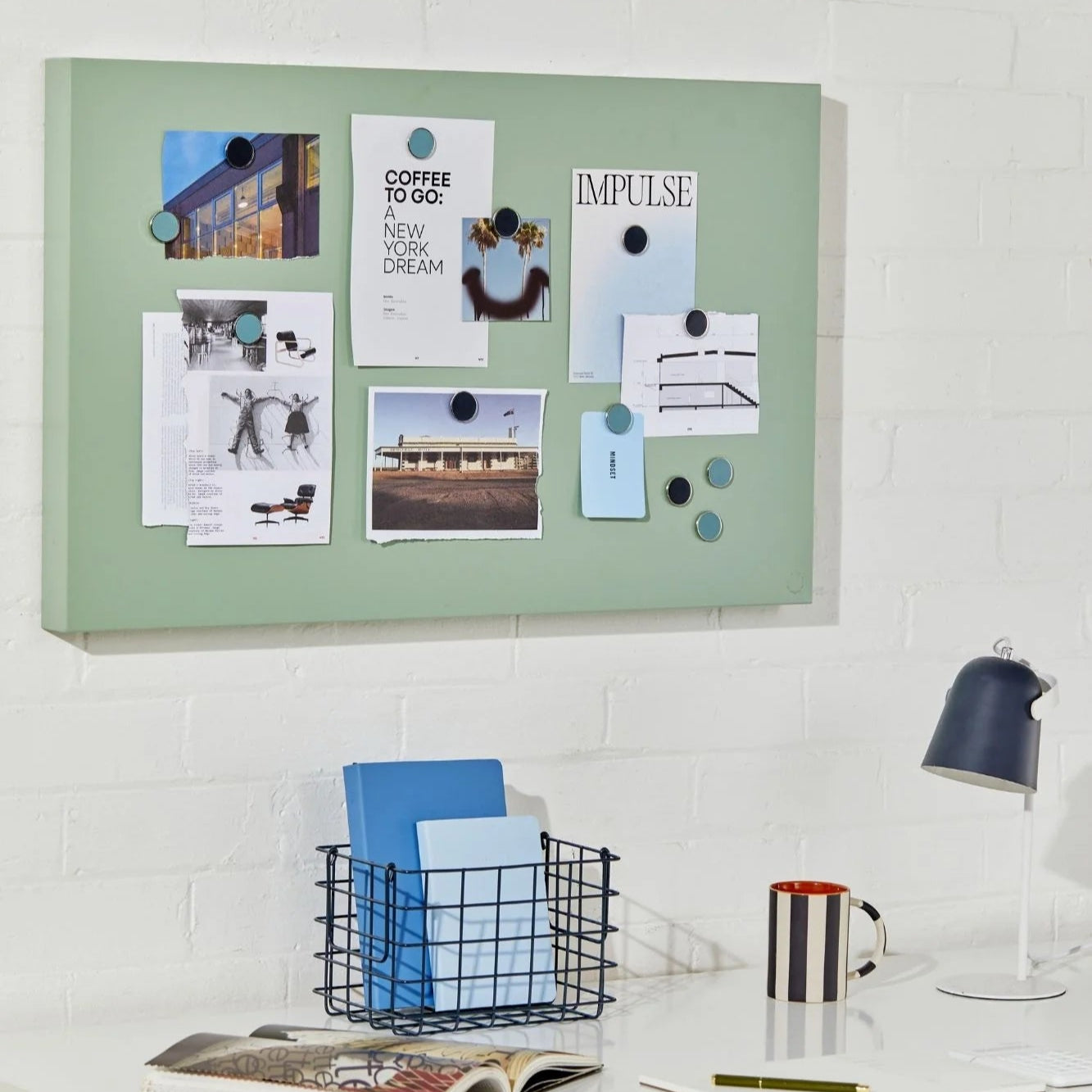 Green magnetic board on a white wall above a desk with office supplies.