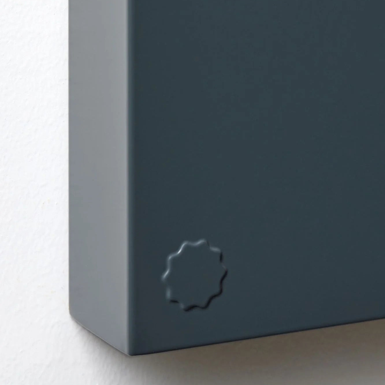 Close-up of a dark gray rectangular object with a circular embossed design on a light gray background