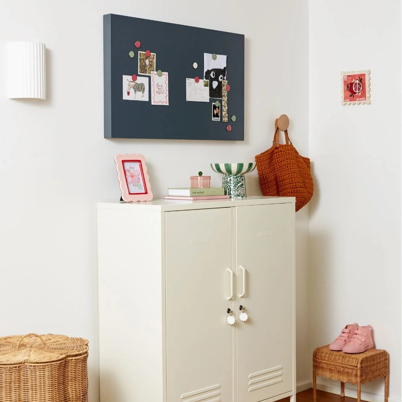 White cabinet with a basket underneath, a blue magnetic board on the wall, and various items on a shelf.