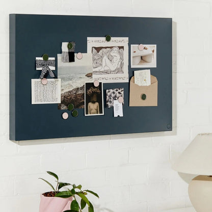 Navy blue magnetic board with various notes and photos on a white wall above a desk.