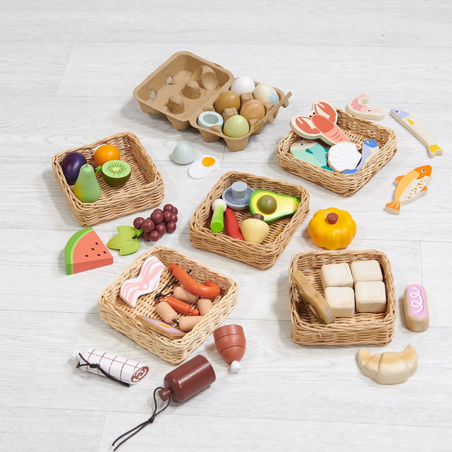 Set of toy food items and baskets on a light wooden surface