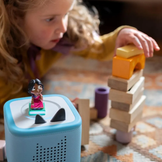 Child playing with a toy block set and a blue electronic device on a patterned surface.