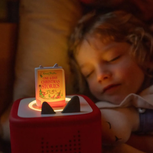 Child lying down with a small red device featuring 'One-Day Christmas Stories' book cover.