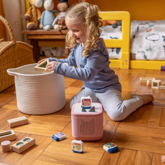 Child playing with toys on a wooden floor in a room with furniture and toys.