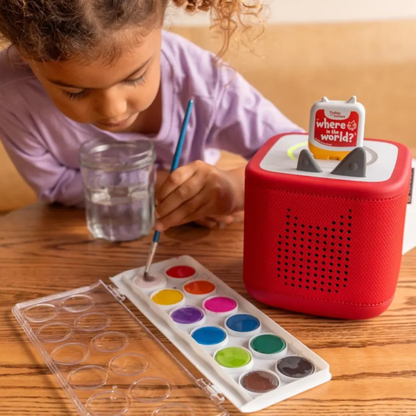 Child painting with watercolors next to a red toy speaker on a wooden table