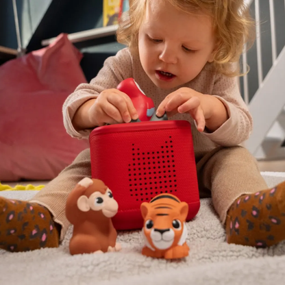 Child playing with a red toy box and animal figurines on a carpeted floor.