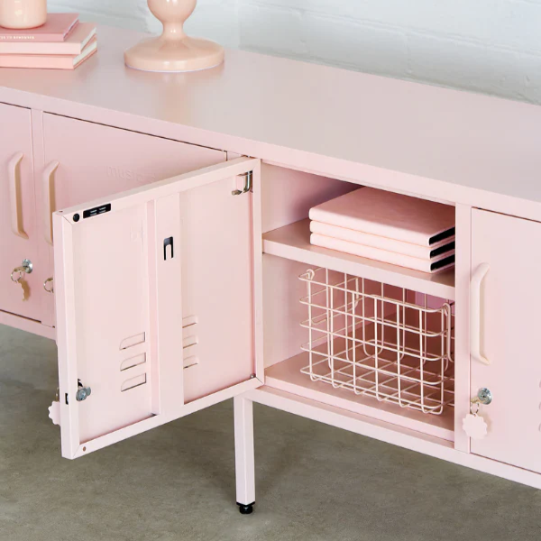 Pink cabinet with open door revealing a wire basket, on a light gray surface.