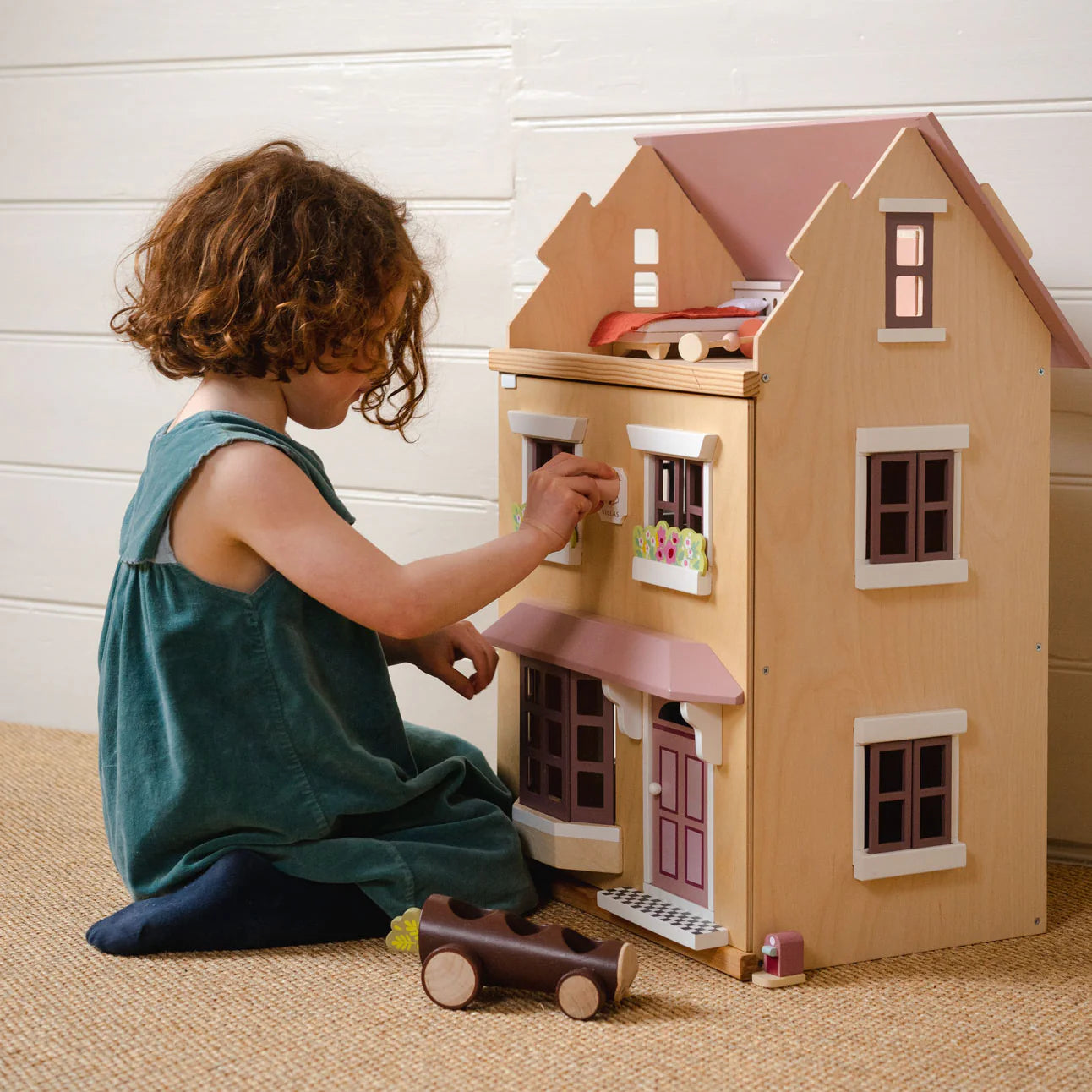 Child playing with a wooden dollhouse and toy car on a carpeted floor.