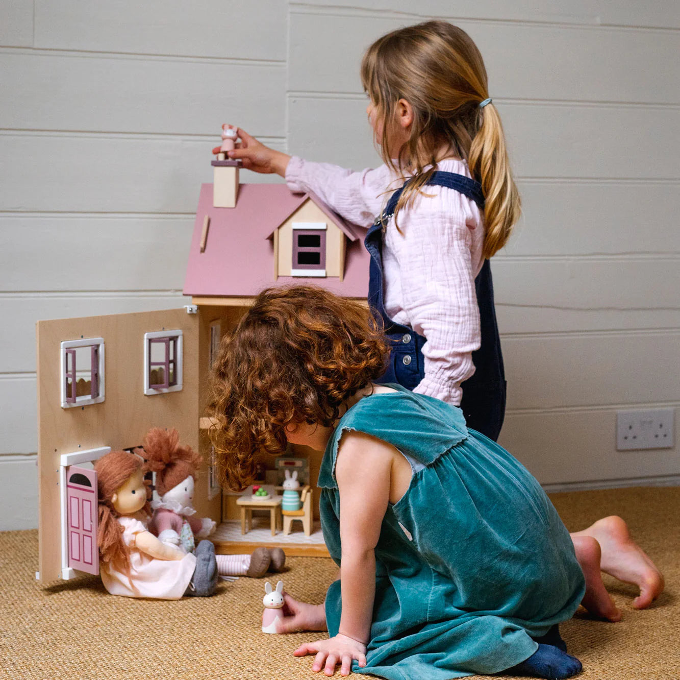 Two children playing with a dollhouse and dolls in a room.