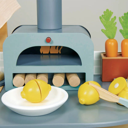 Toy kitchen set with oven, fruits, and vegetables on a table.