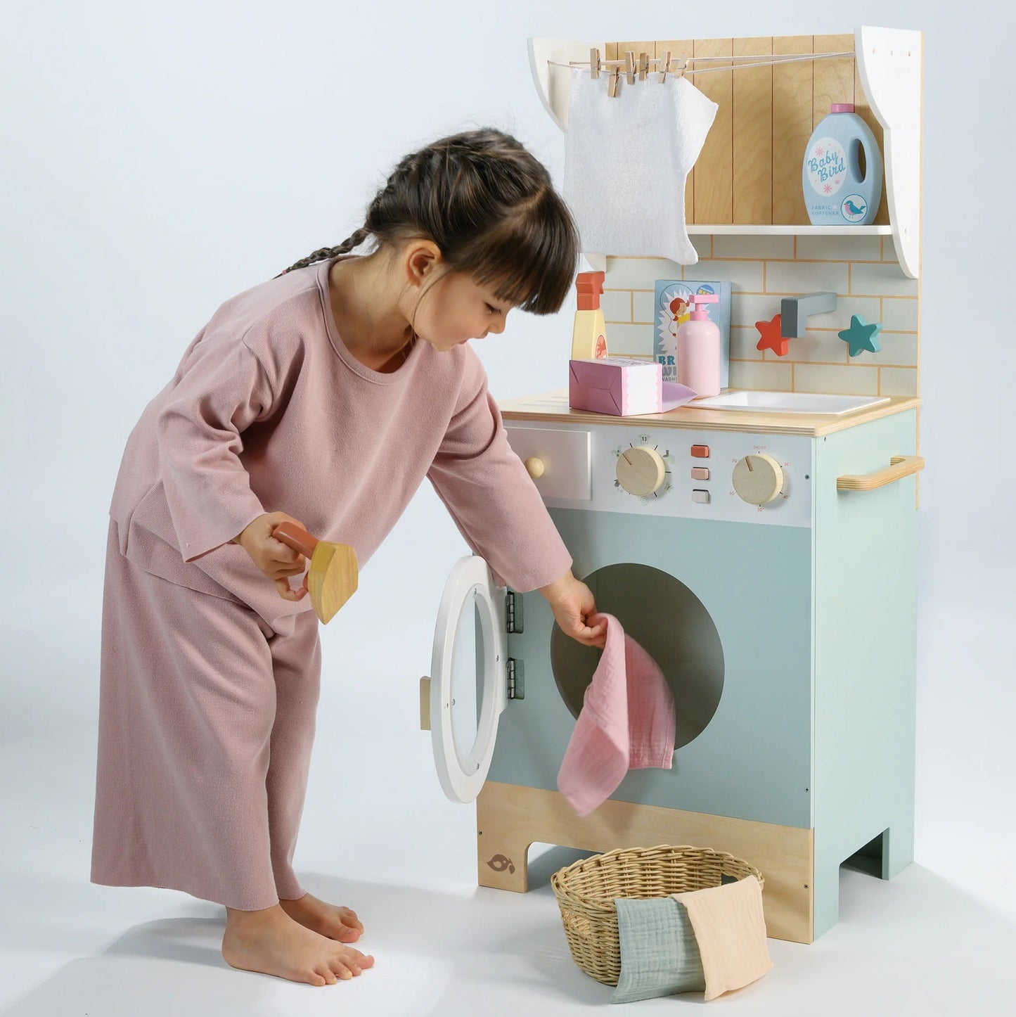 Child playing with a toy washing machine and dryer set on a light background