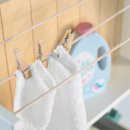 White baby clothes hanging on a line with wooden clips against a light-colored wall.