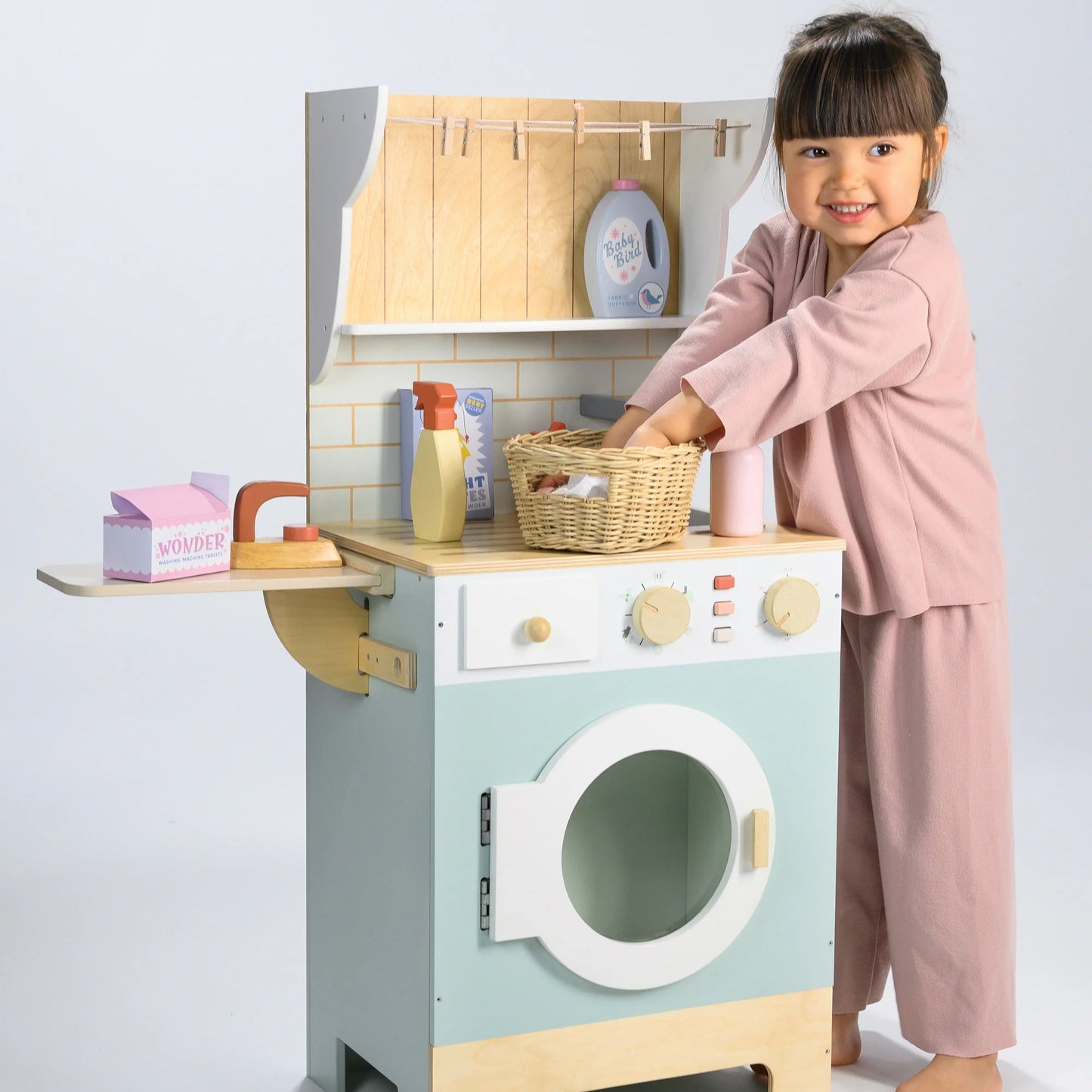 Child playing with a toy washing machine and dryer set on a light gray background