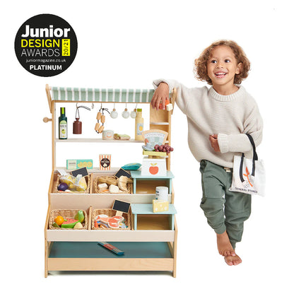 Child standing next to a toy kitchen set with Junior Design Awards logo.