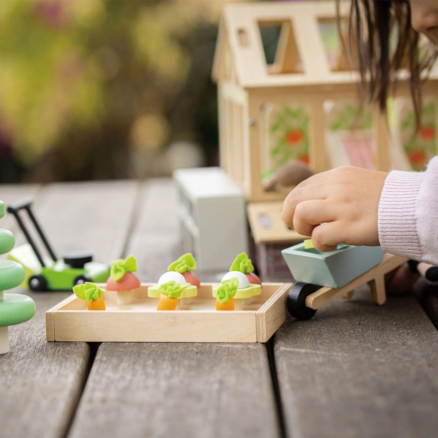 Child playing with a toy train set on a wooden table outdoors.