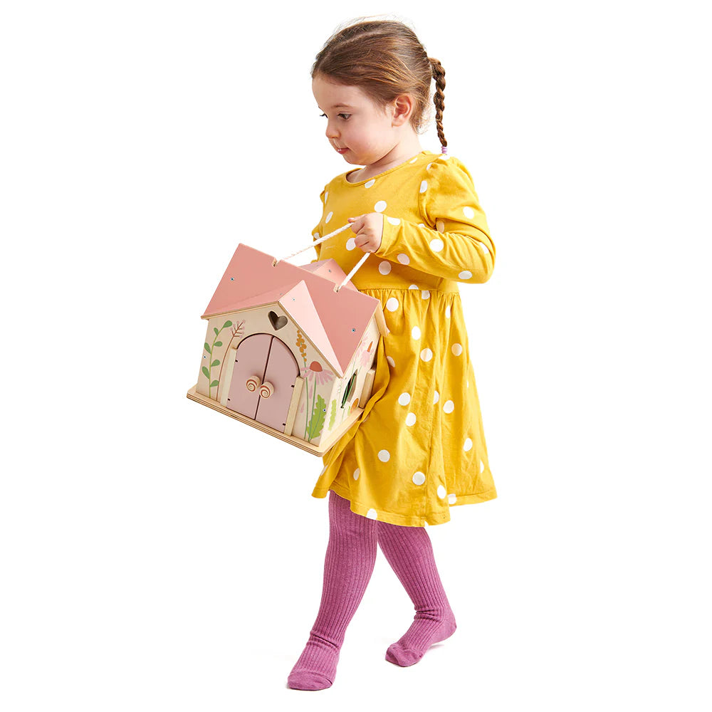 Child in a yellow dress with white polka dots holding a pink fairy house against a white background
