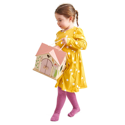 Child in a yellow dress with white polka dots holding a pink fairy house against a white background