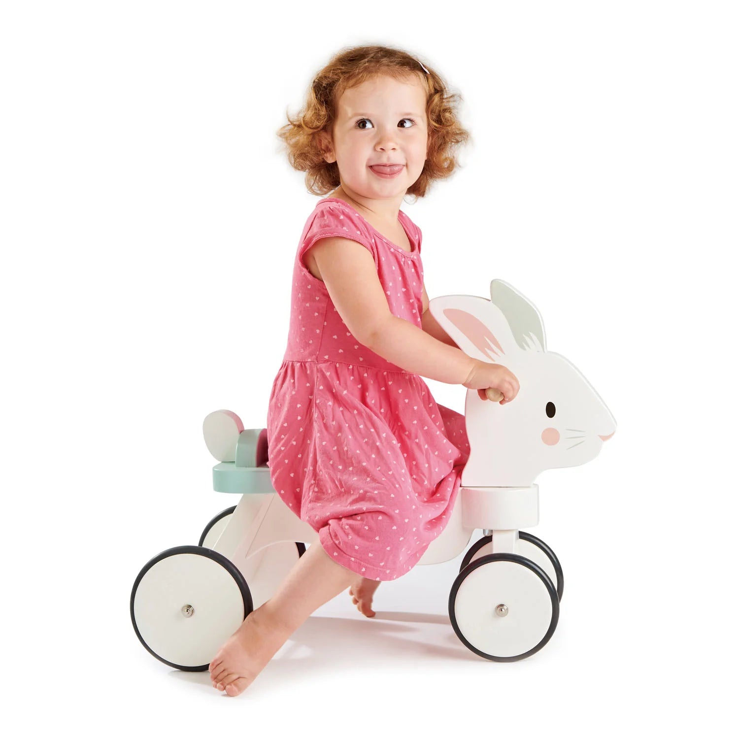 Child in a pink dress riding a white toy horse with a smiling expression on a white background
