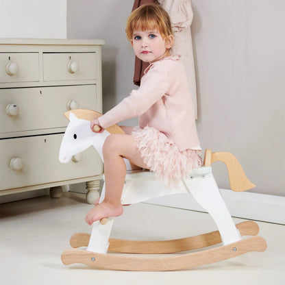 Child sitting on a wooden rocking horse in a room with a dresser and hanging clothes.
