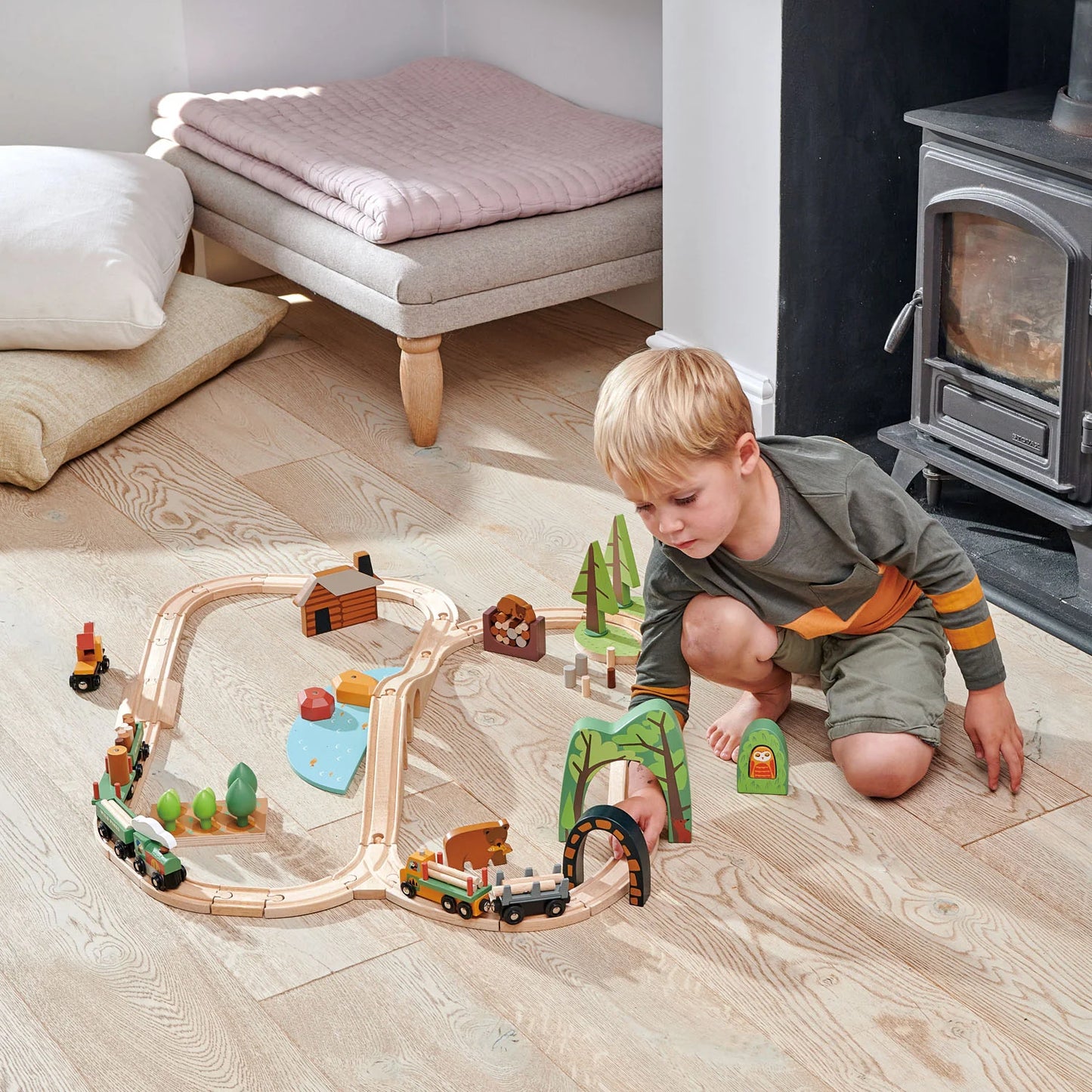 Child playing with a wooden train set on a wooden floor in a cozy living room.