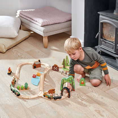 Child playing with a wooden train set on a wooden floor in a cozy living room.