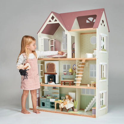 Young girl playing with a wooden dollhouse on a plain background