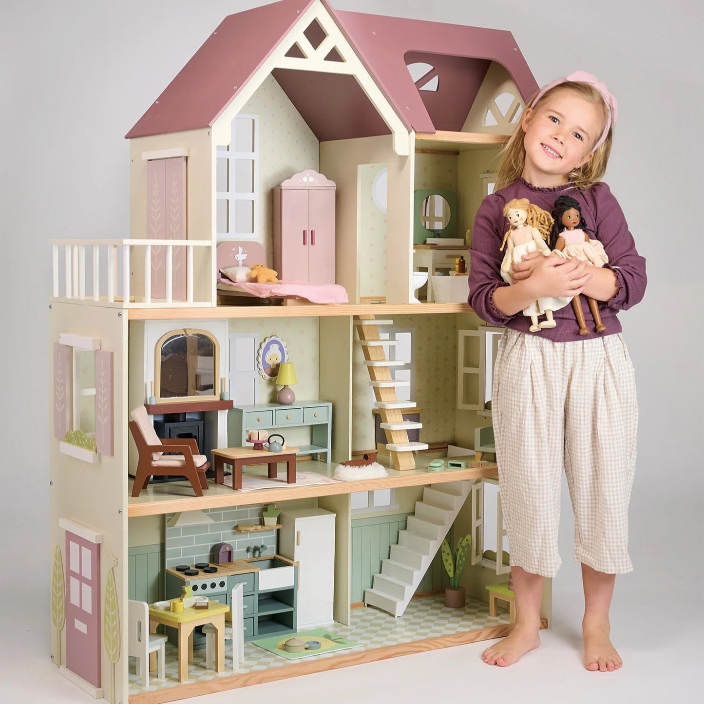 Child with a large wooden dollhouse and toys on a plain background