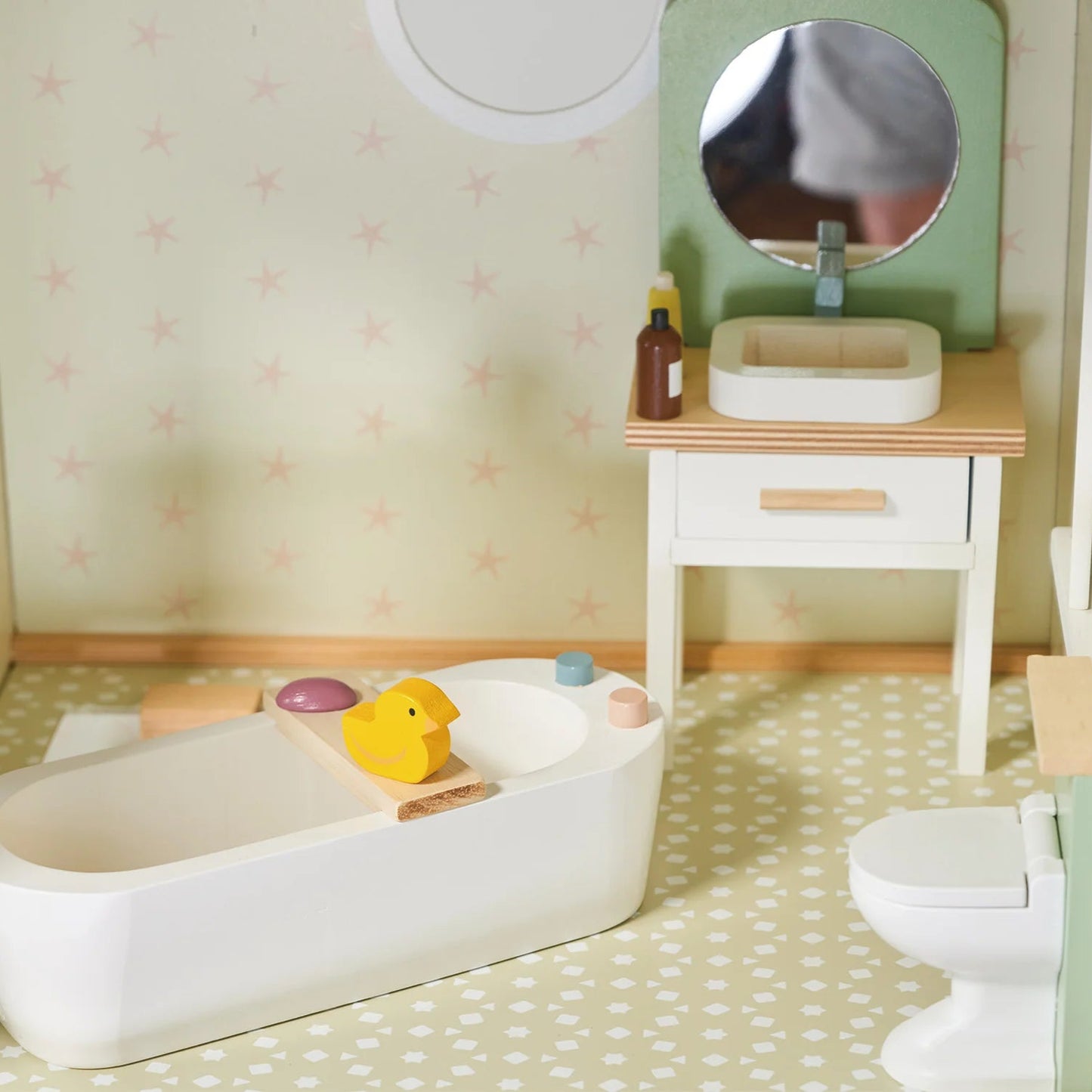 Miniature bathroom set with bathtub, sink, and toys on a checkered floor.