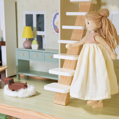 Dollhouse scene with a doll in a yellow dress standing on a staircase.