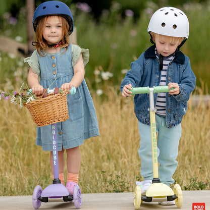 Two children on scooters with helmets in a natural setting