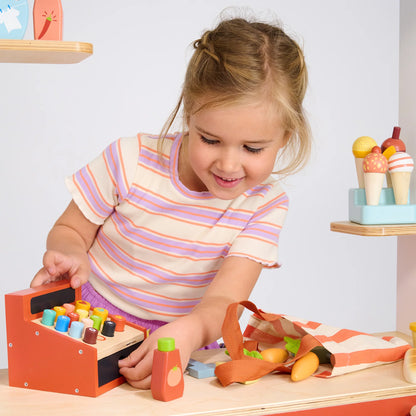Child playing with a wooden toy cash register and blocks on a table.