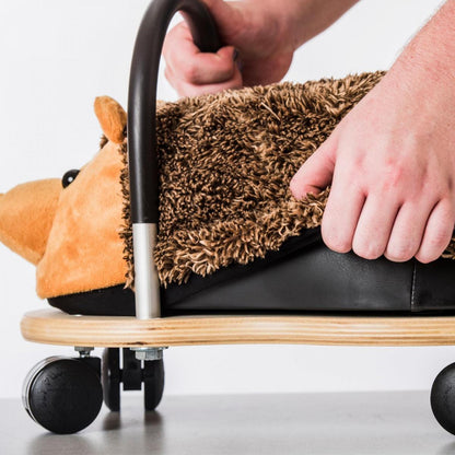 Person using a small wooden scooter with a plush toy on a white background