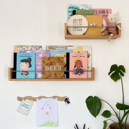 Wooden shelves with books and stationery on a white wall, next to a plant.