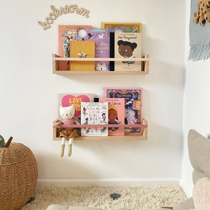 Wooden shelves with children's books on a white wall, with a soft rug and toy in the foreground.