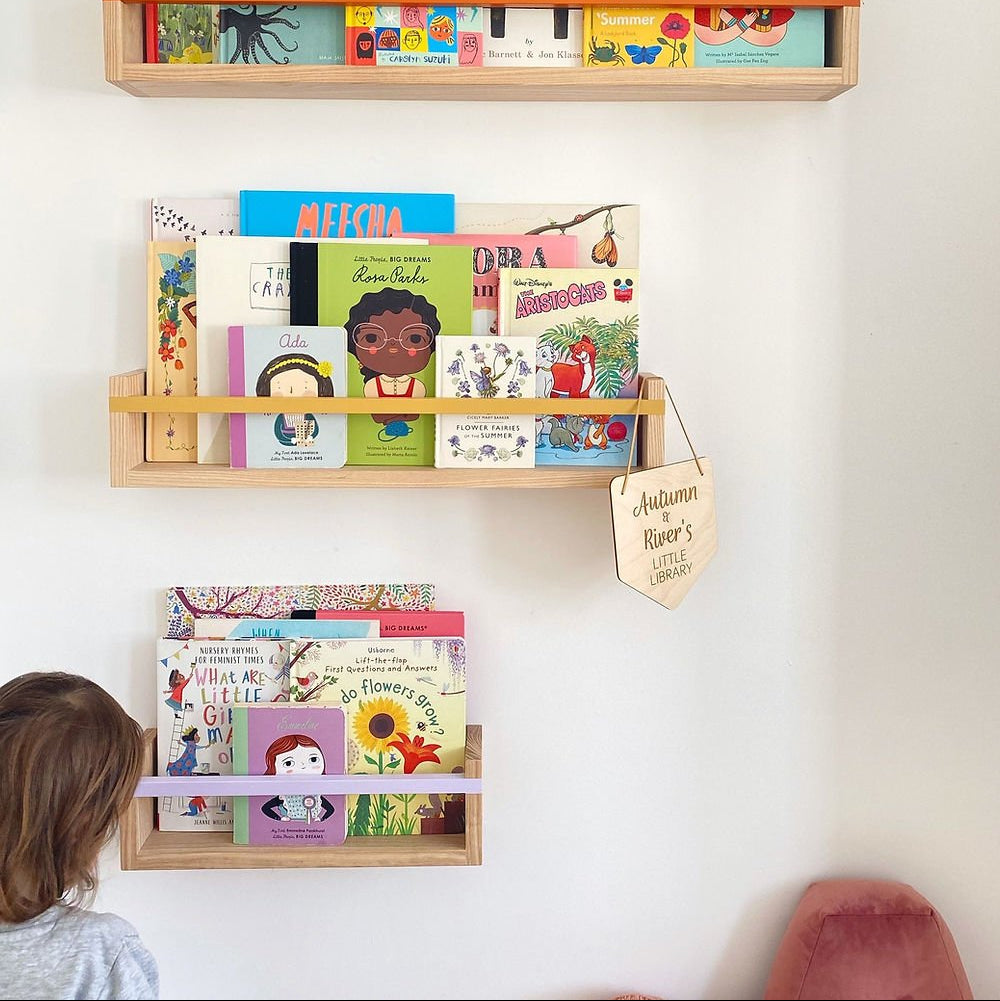 Children's books on wooden shelves against a white wall