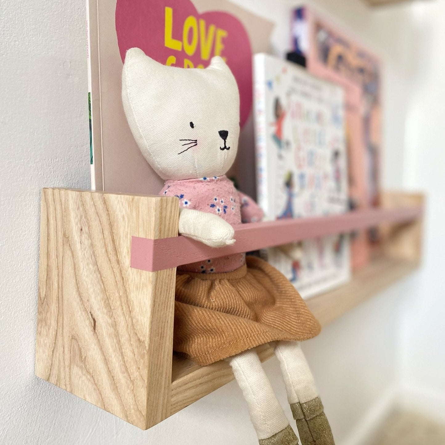 Toy cat with a dress on a wooden shelf with books in the background