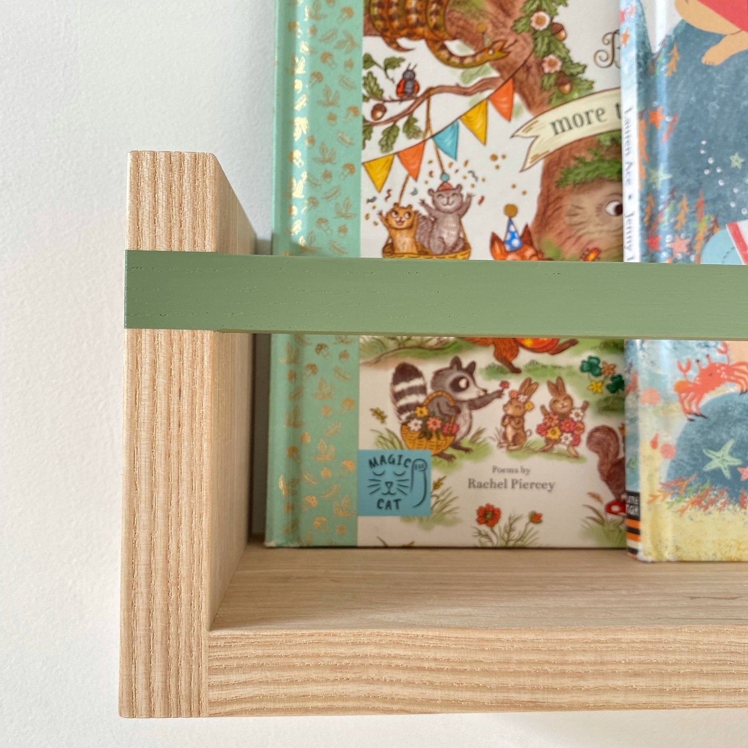 Children's books with colorful covers on a wooden shelf with a green holder.