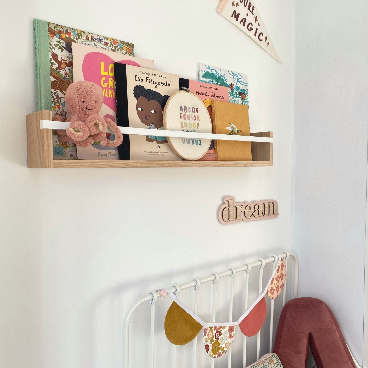Children's room with books on a shelf, a bed with decorative pillows, and a 'dream' wall decoration.