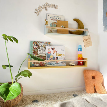 Children's room with a shelf displaying books and toys, a plant, and a decorative letter 'R'.