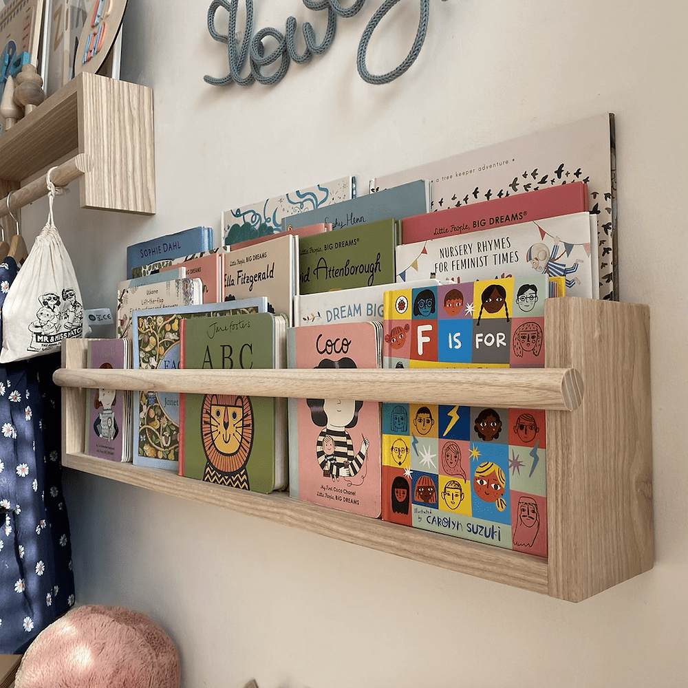 Wooden shelf with children's books and toys on a wall with decorative text.