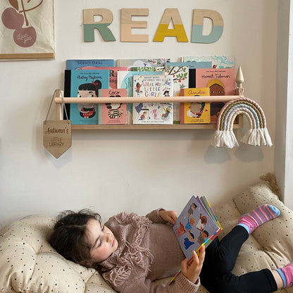 Child reading a book on a couch with a wall display of books and 'READ' sign.