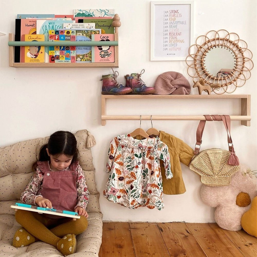 Child reading a book on a couch in a playroom with shelves and toys.