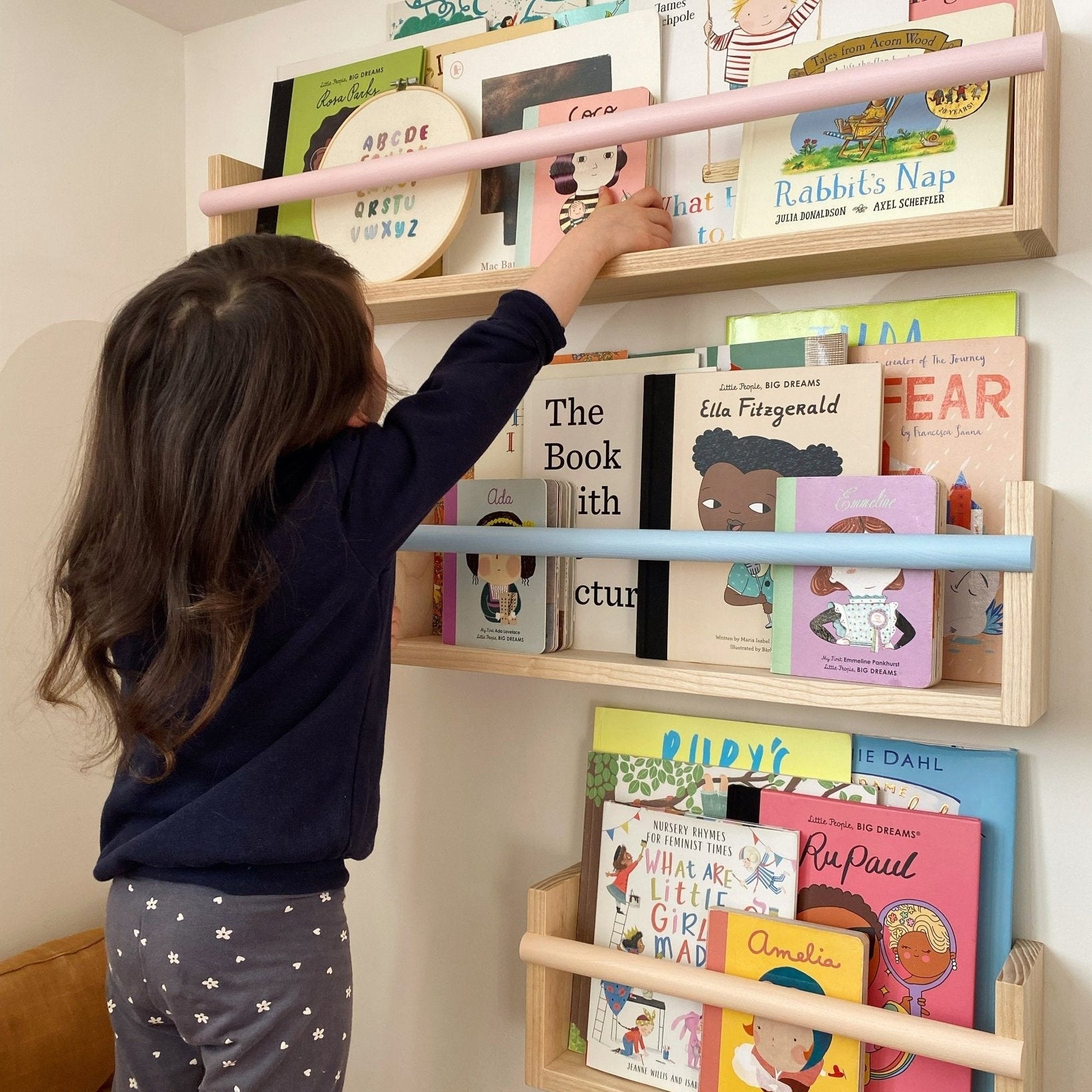 Child reaching for a book on a wall-mounted children's bookshelf filled with books.