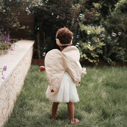 Child in angel costume with wings standing in a garden with bubbles