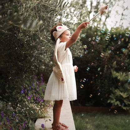 Young girl in a white dress blowing bubbles in a garden setting