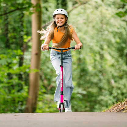 Young girl riding a pink scooter in a forested area