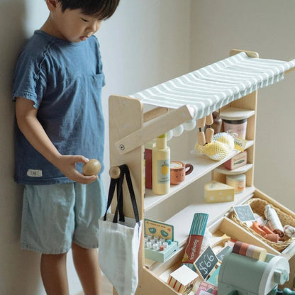 Child playing with a toy kitchen set against a plain wall