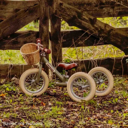 Children's balance bike with basket against a wooden fence in a natural setting